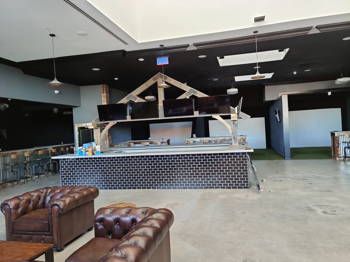 Commercial entertainment venue lounge area with leather seating and multi-screen bar display