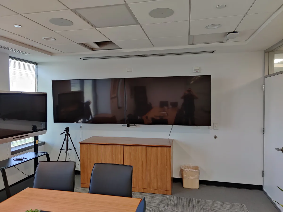 Close-up of wall-mounted conference displays with credenza and video tripod in a corporate boardroom