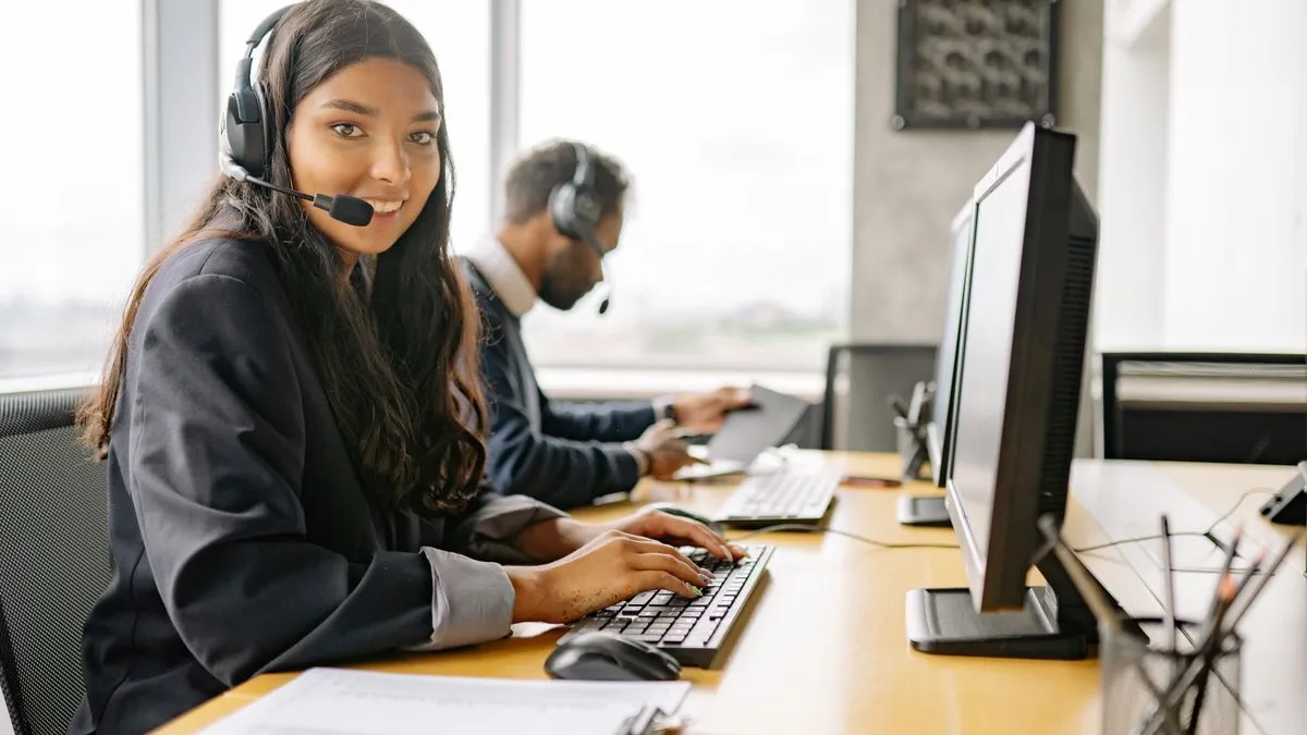 Two office workers taking calls on headsets at their desks in a bright modern office