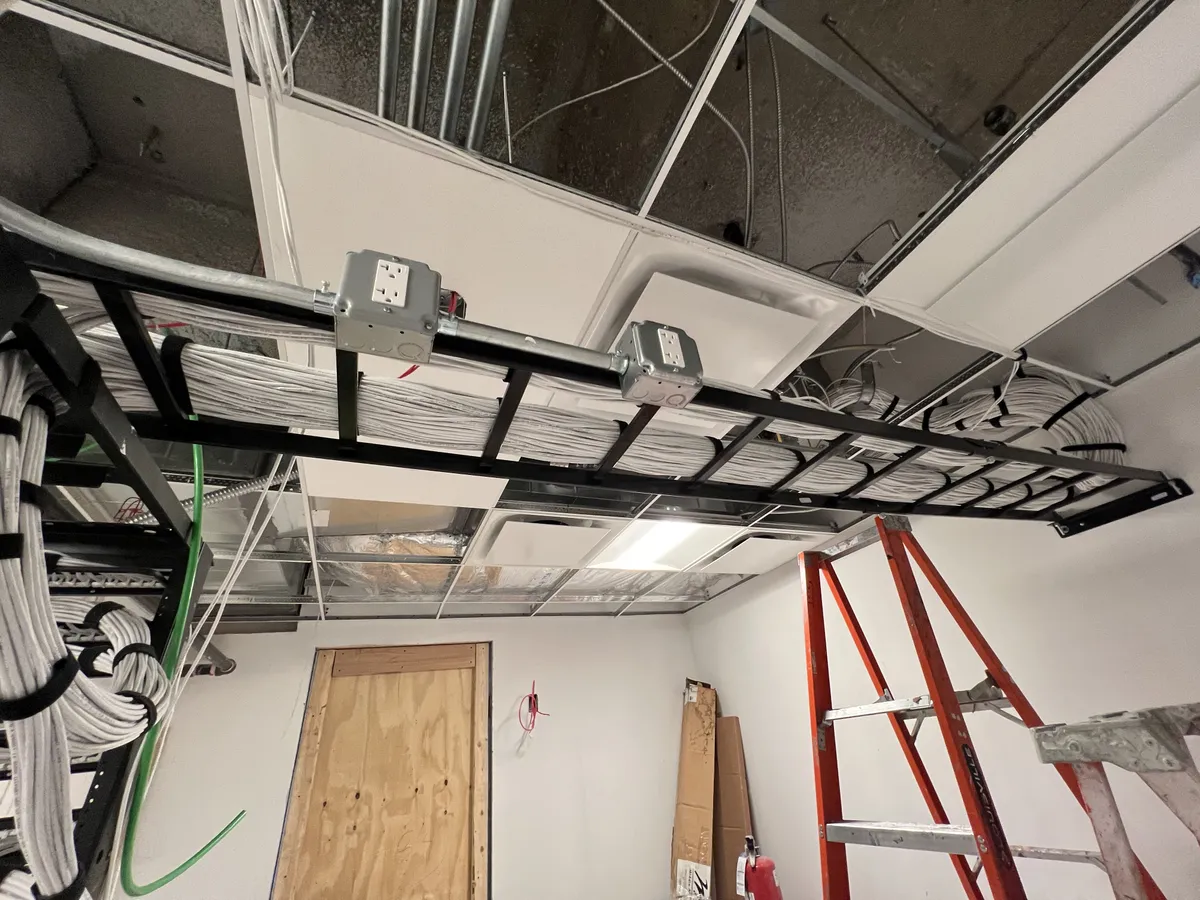 MDF room wide view — overhead ladder rack loaded with bundled cable runs, junction boxes, and red ladder during buildout