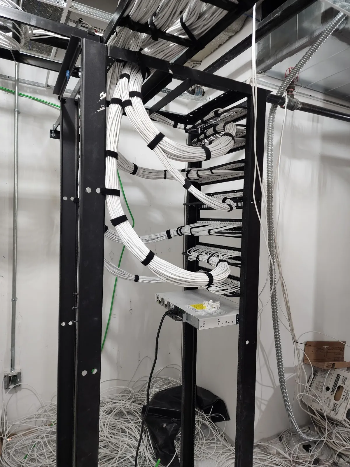 MDF room during rough-in — two-post rack with cable waterfall, conduit runs, and bare walls