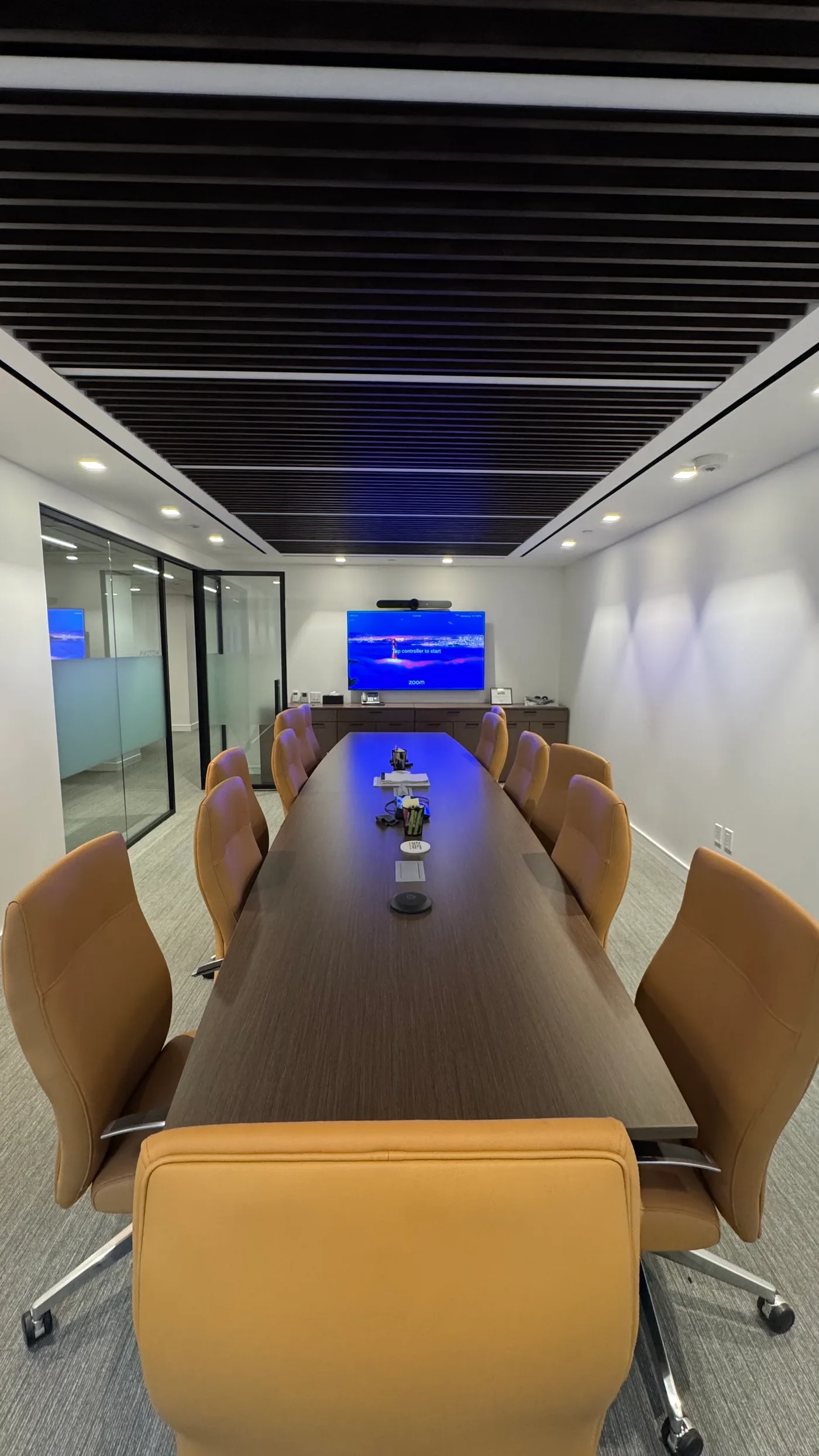 Long boardroom with a Zoom Room video bar and wall display under a wood-slat ceiling