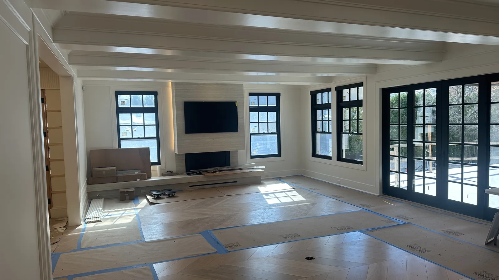 High-end great room under construction with coffered beam ceiling, chevron wood floor, and a TV mounted on a stone fireplace feature wall