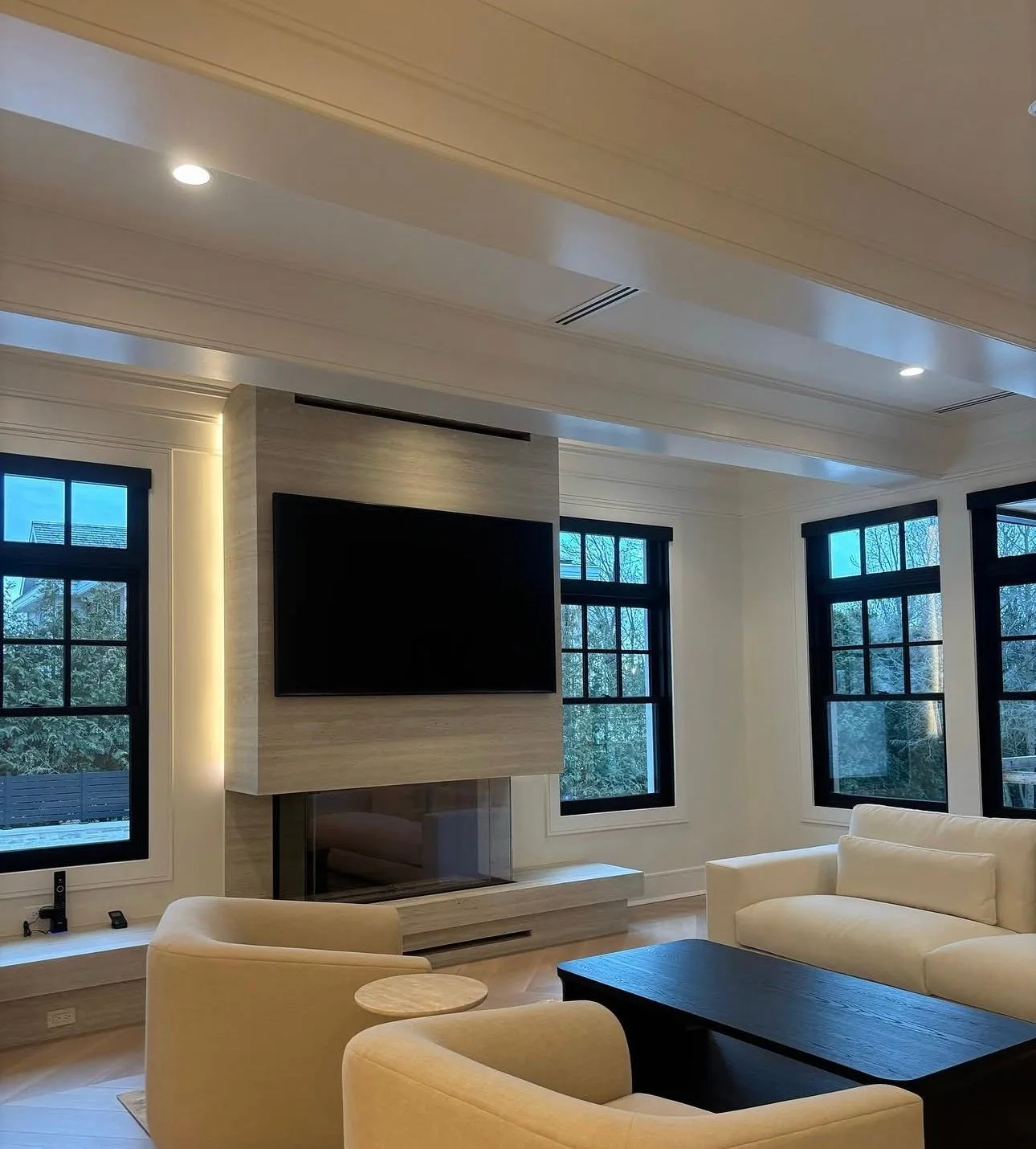 Finished great room with a TV on a travertine feature wall over a linear fireplace — the room audio is Sonance Invisible Series speakers plastered into the walls
