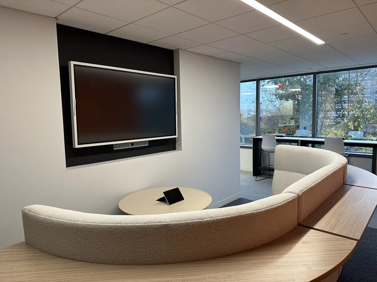 Cisco Webex Board on dark panel surround with curved sofa seating and touch controller