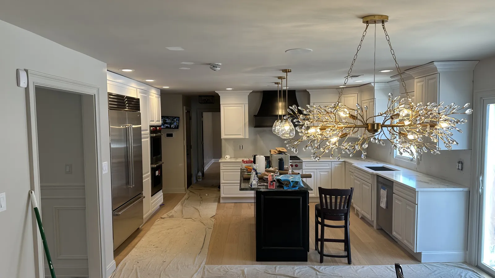 Kitchen renovation in progress with a crystal branch chandelier, brass pendants, in-ceiling speakers, and white cabinetry