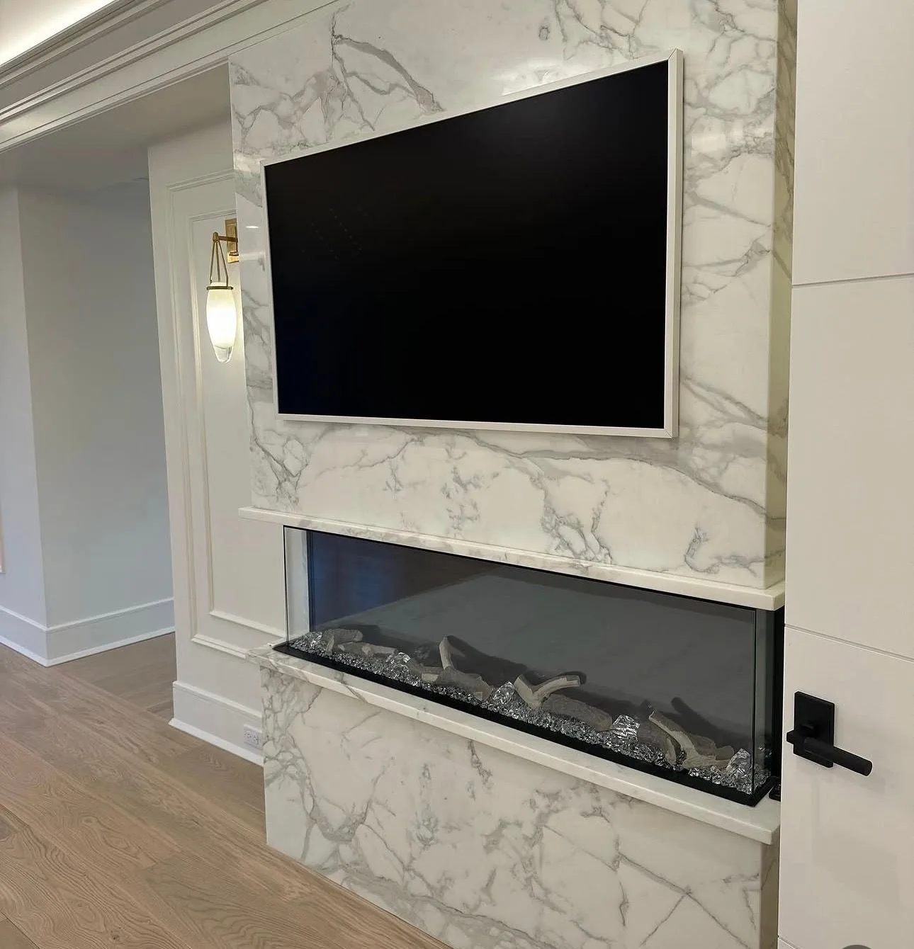TV mounted flush on a book-matched marble feature wall above a linear glass fireplace