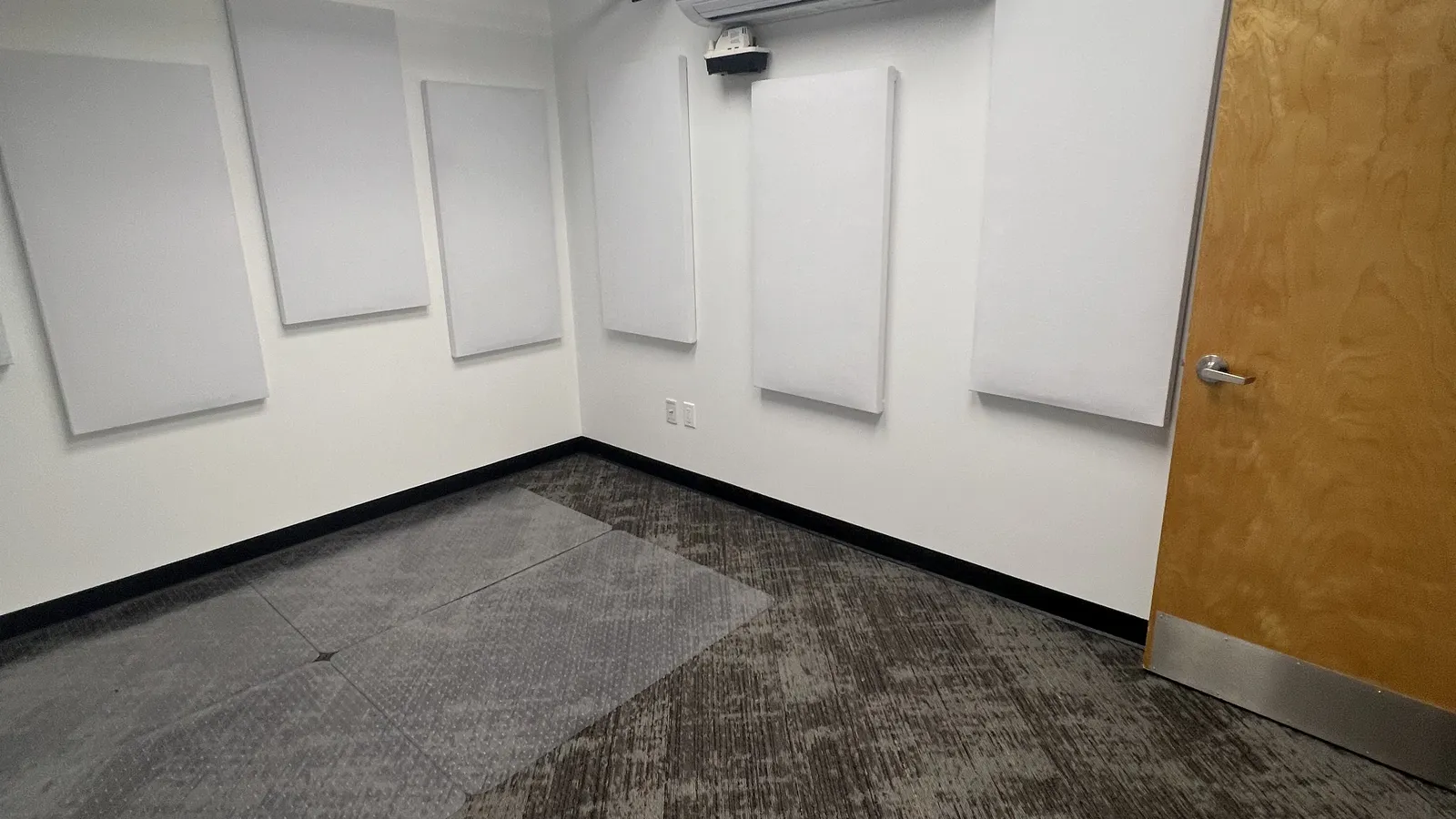 Office studio room with white acoustic wall panels, a ceiling-mounted projector, a mini-split, and an overhead cable ladder rack