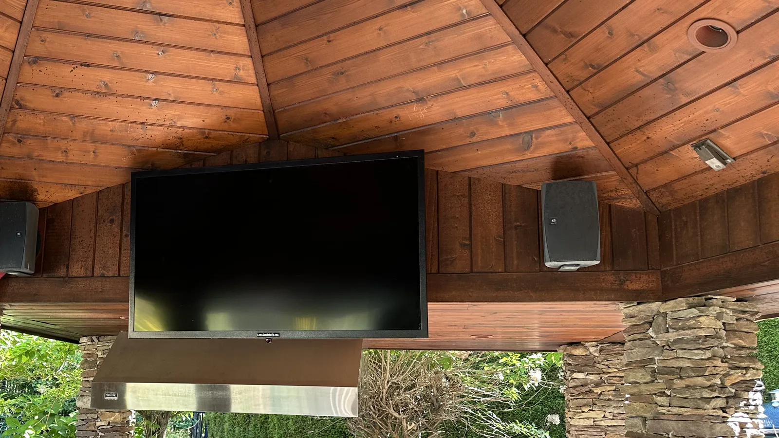 Backyard gazebo with a mounted TV and outdoor surround speakers over the outdoor kitchen