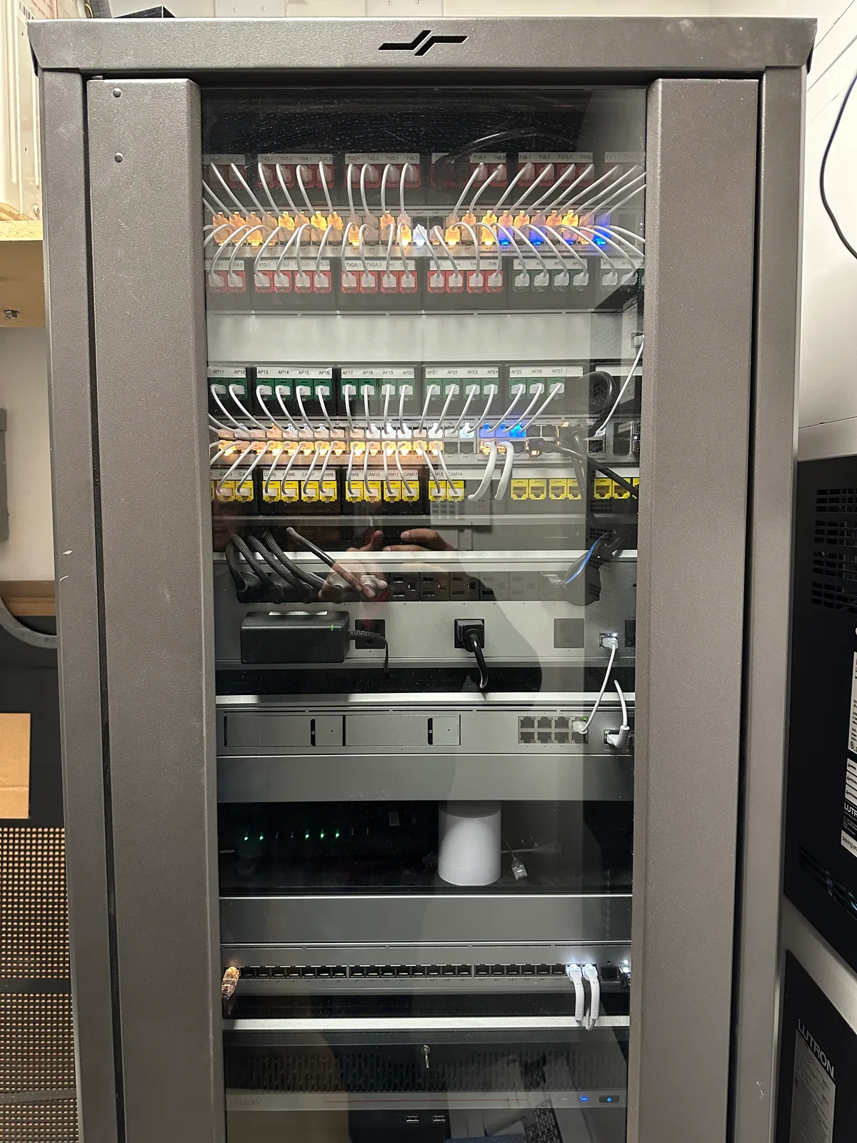 Smart-home equipment rack behind a glass door with patch panels, switches, and streaming gear